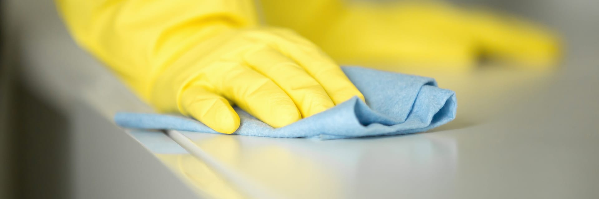 a hand in a rubber glove is cleaning a surface with a blue piece of cloth.